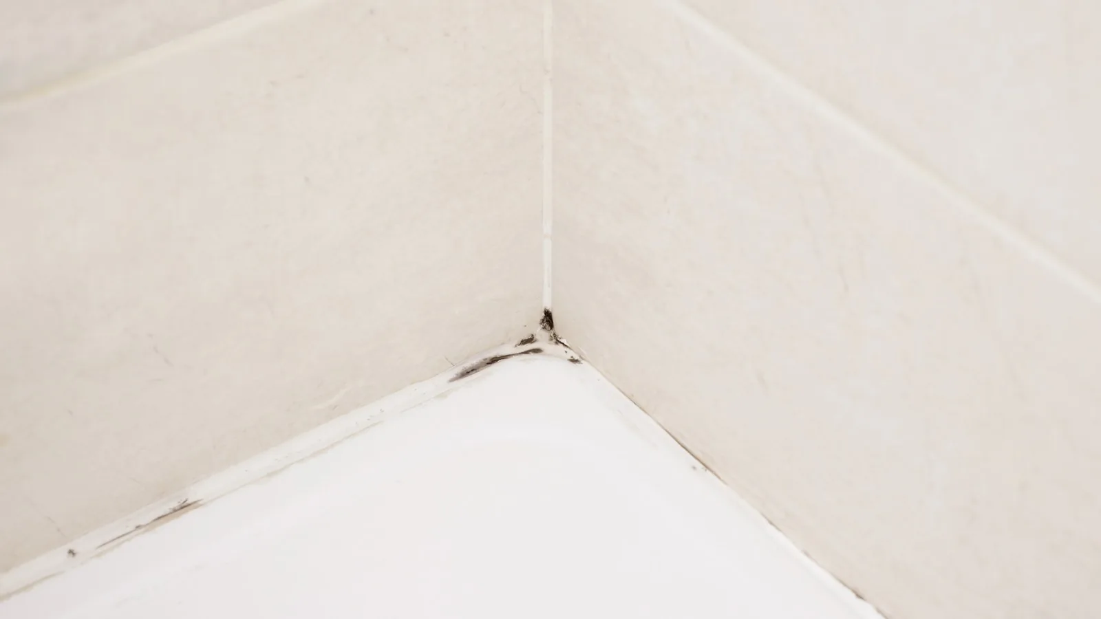 A bathroom corner where the silicone sealant has started to stain black at the joint.