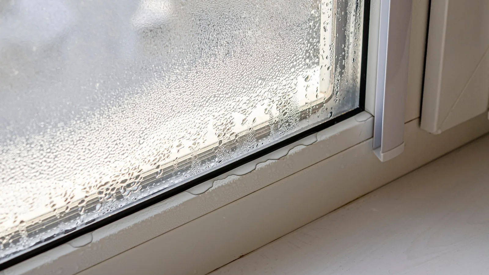 Heavy condensation running down the inside of a window pane on a cold morning.
